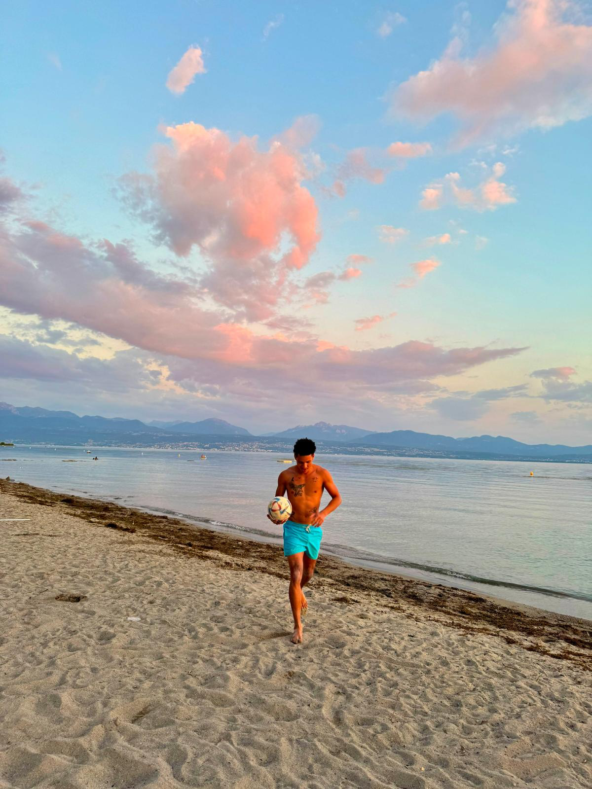 Emiliano Alves na praia ao pôr do sol, segurando uma bola